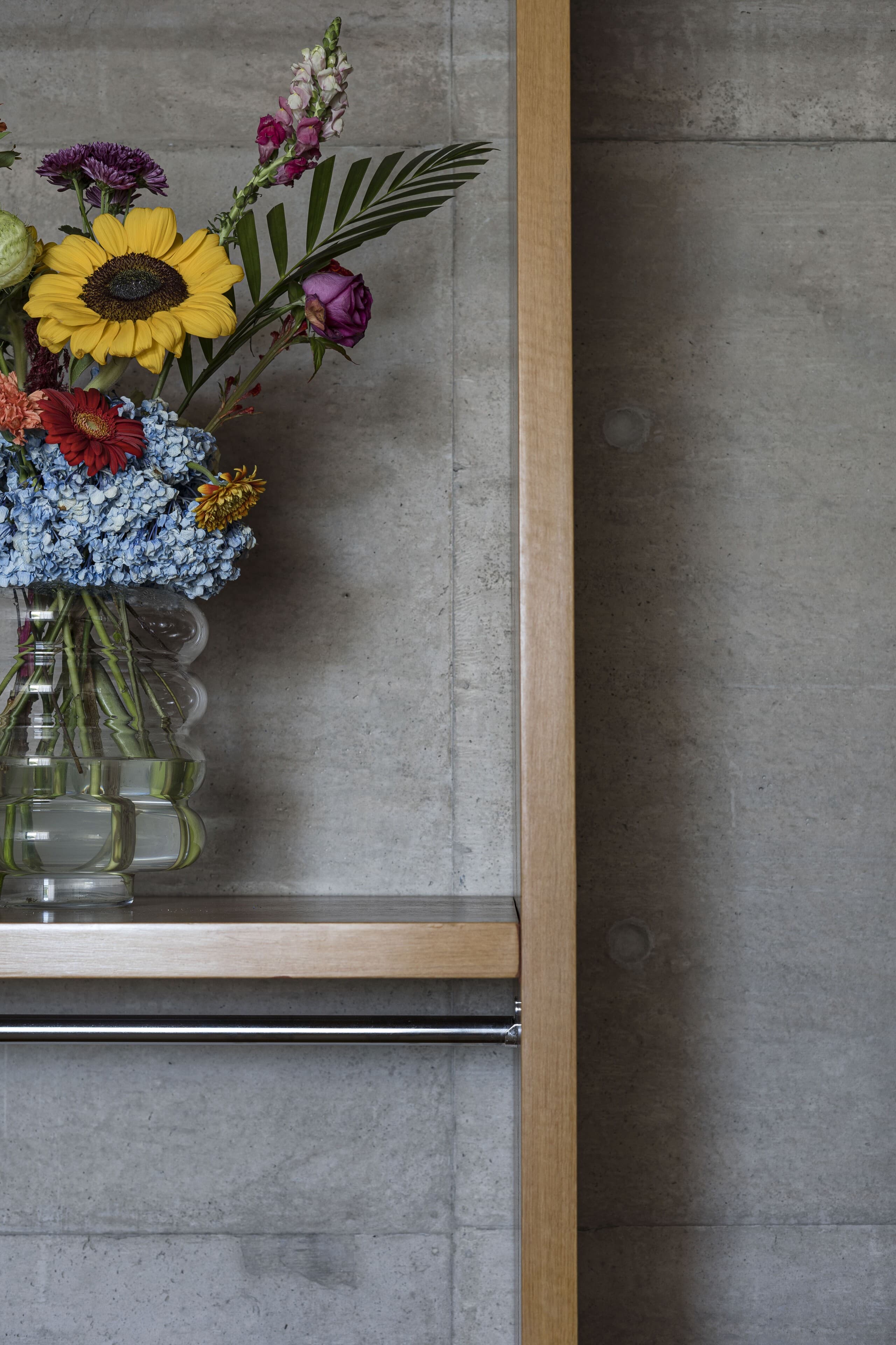Sunflowers and hydrangeas in a glass vase against board-formed concrete and timber.