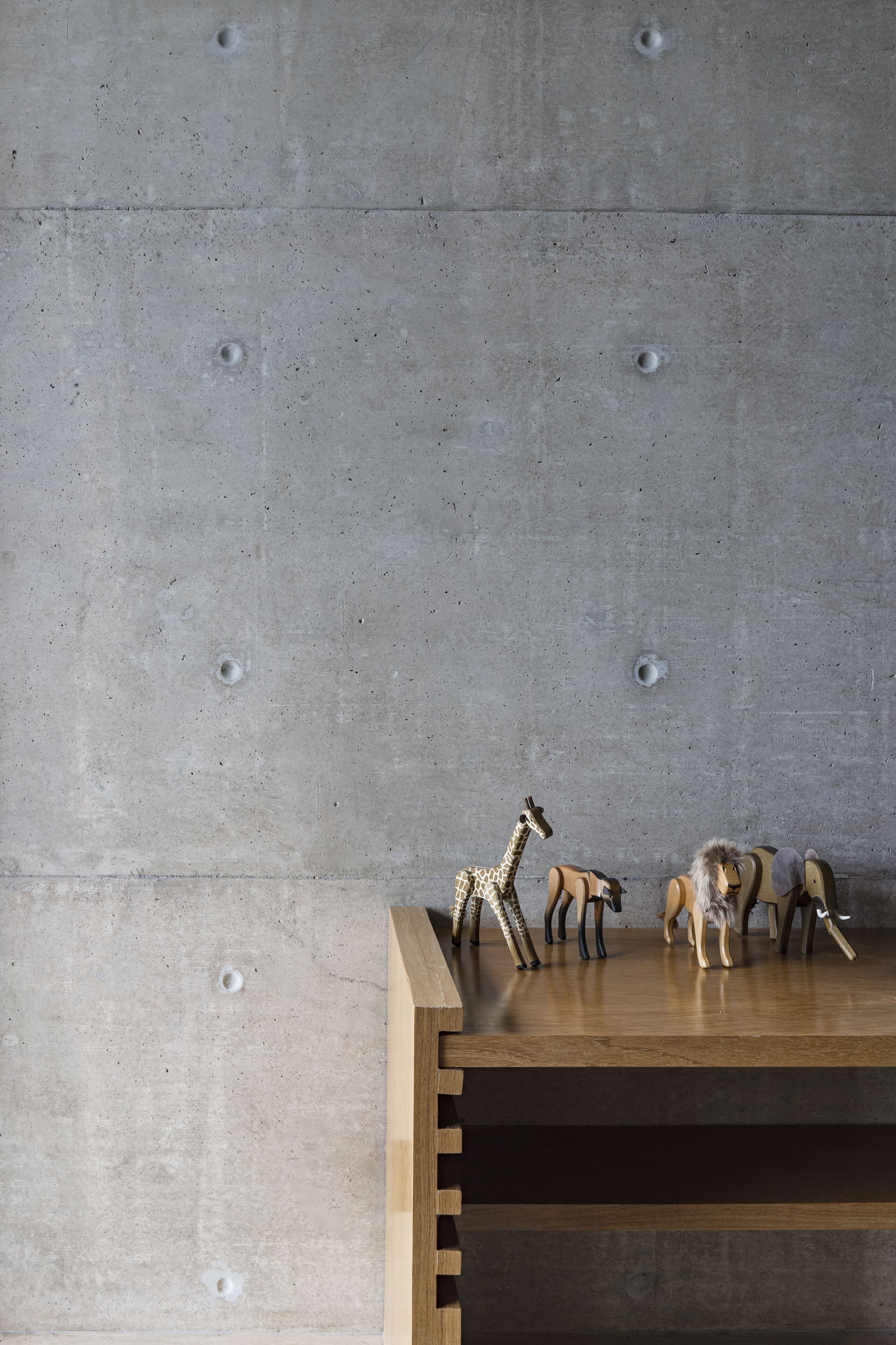 Small carved wooden horses on a timber console against a concrete wall.